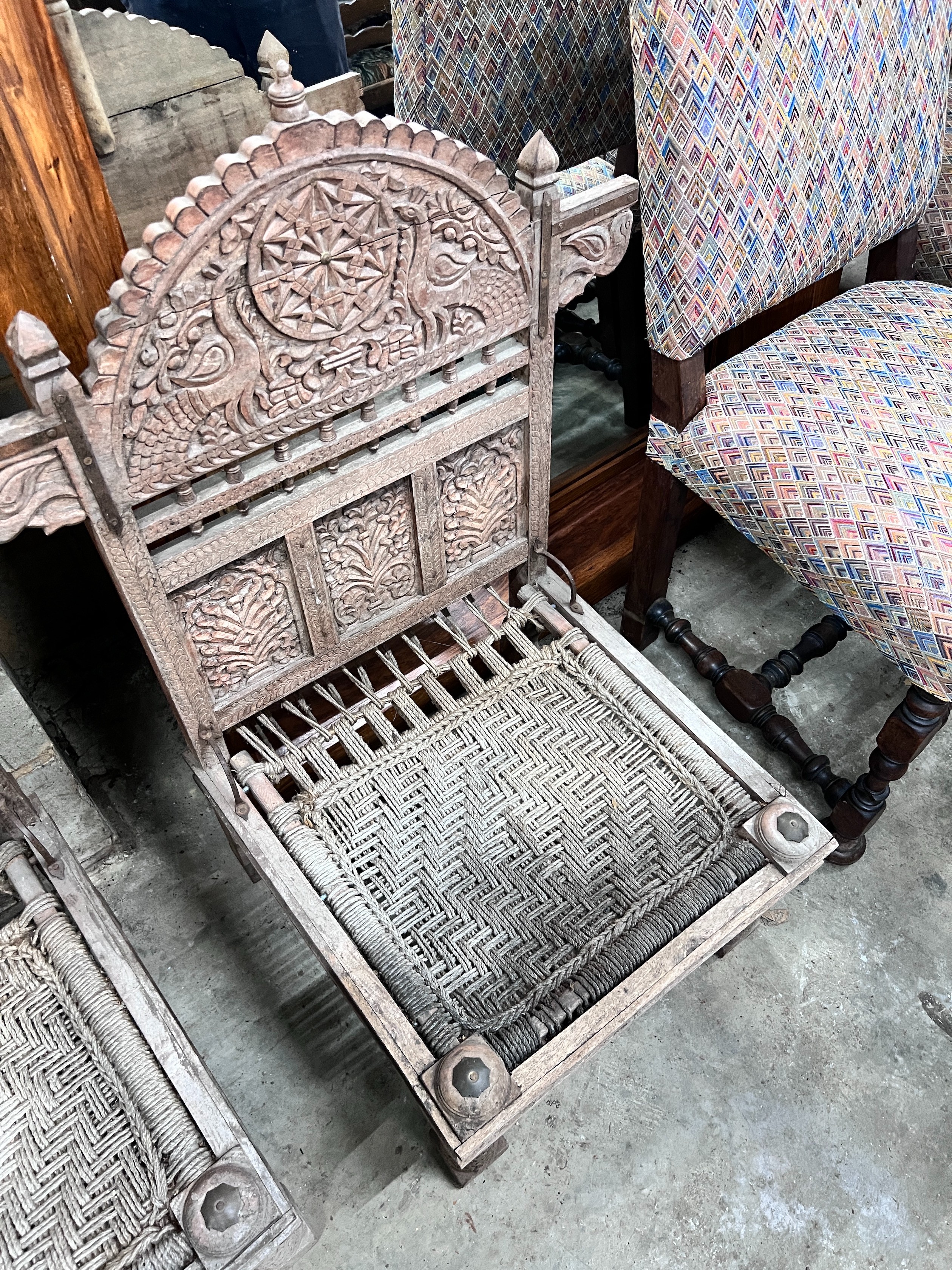 A pair of Indian carved teak low chairs with ropework seats, width 69cm *Please note the sale commences at 9am.